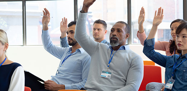 Group of people in meeting, all with their hands raised.